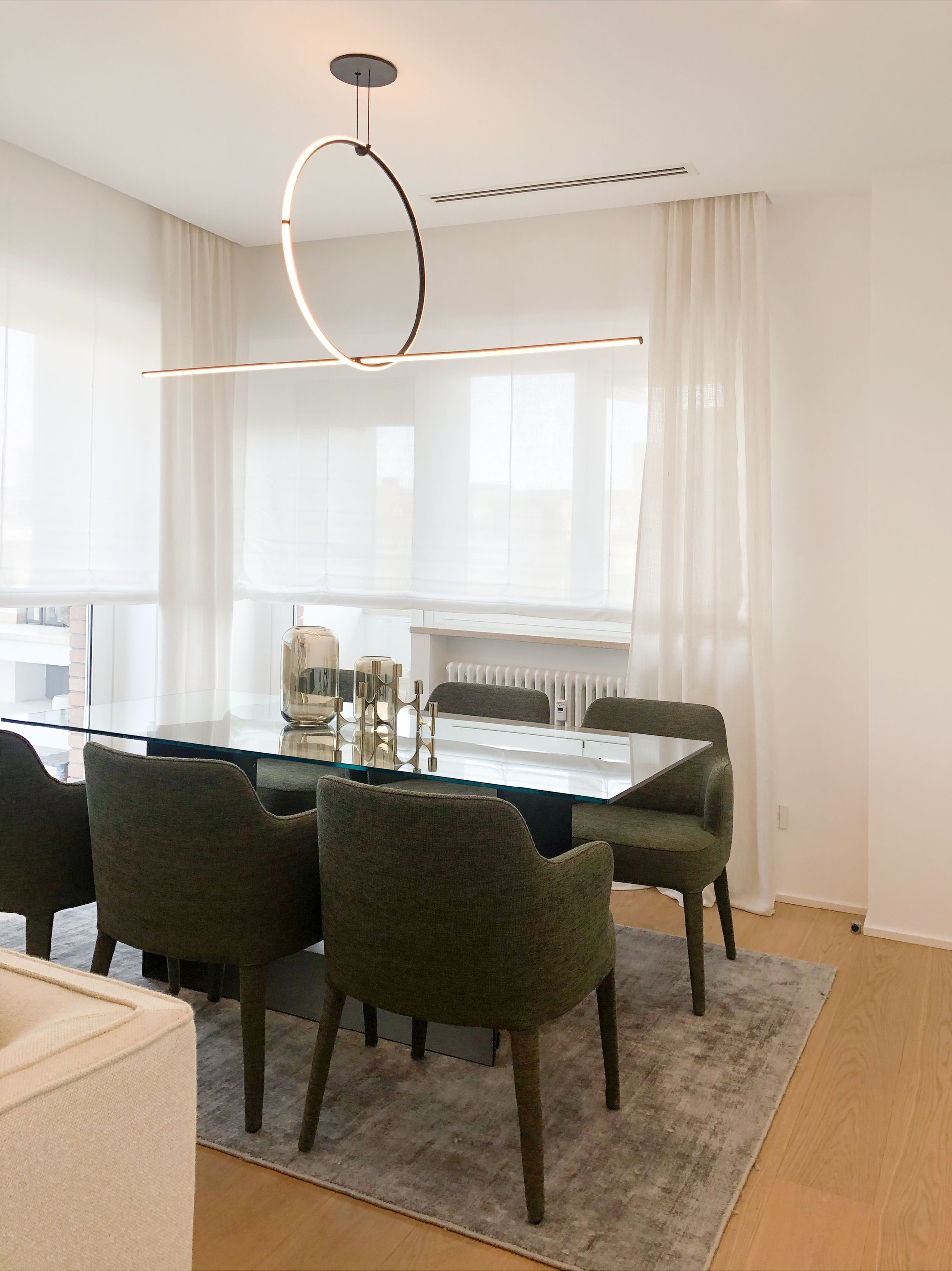 Stylish dining room with glass table, green chairs and circular pendant lighting